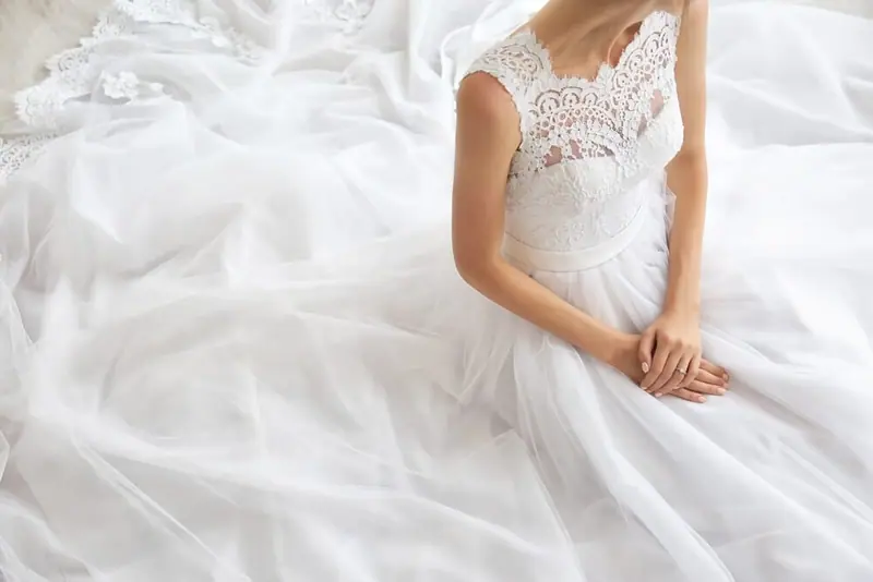 Bride sitting on white bedding in a lace wedding dress